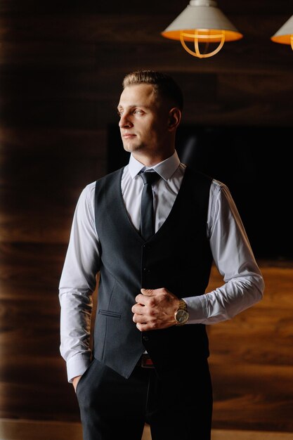 a man in a vest and tie stands in front of a wall