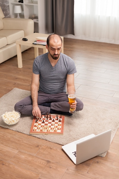 Man in a video call playing chess with friends and holding beer glass during self isolation.