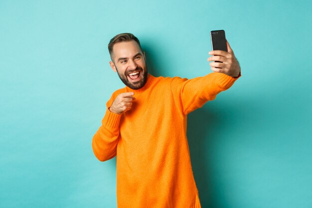  man video calling on mobile phone, taking selfie and pointing at smartphone camera