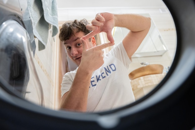 Man view from washing machine inside Male does laundry daily routine Made a photo frame with fingers