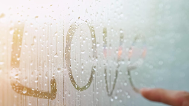 Man vinger schrijft woord liefde op raam bedekt met mist