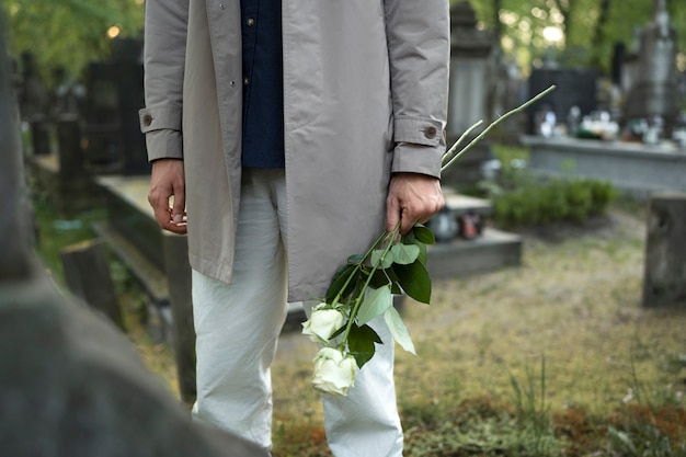 Foto uomo in visita al cimitero con rose bianche