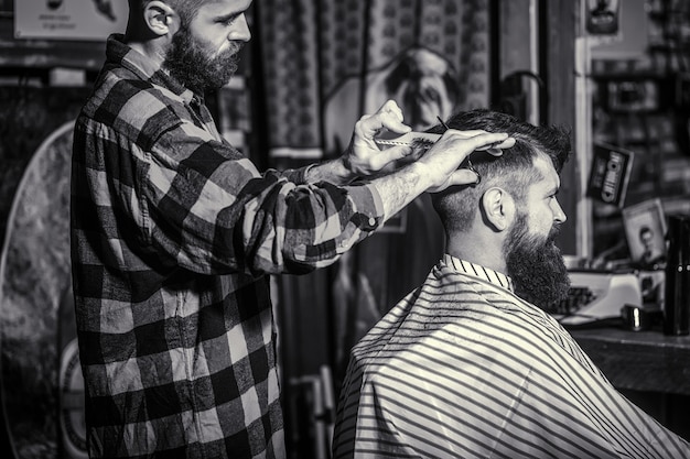 Man visiting hairstylist in barbershop. Barber scissors. Black and white. Bearded man in barber shop.