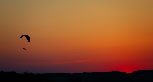 Man vlucht op een paraglider in een wolkenloze hemel bij zonsondergang