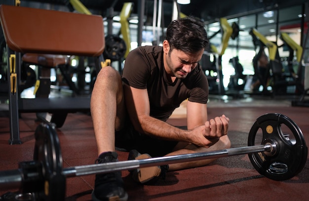 Man voelt pijn in zijn pols na training tillen met barbell in fitness gym