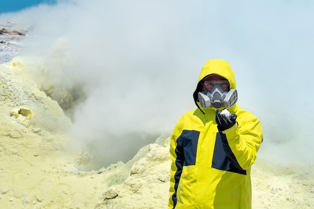 噴気孔を背景に男性の火山学者が鉱物のサンプルを示しています