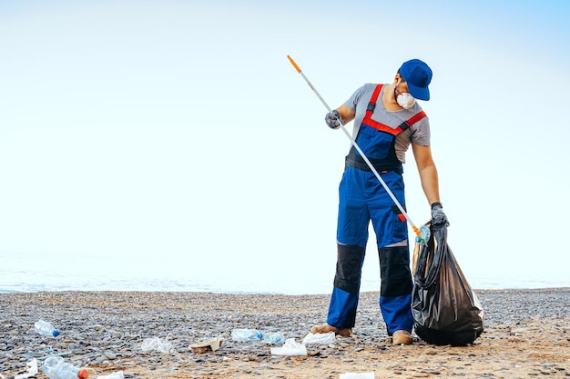 사진 리치 익스텐더 스틱으로 해변에서 쓰레기를 수집하는 자원 봉사자