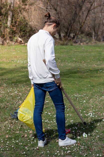 Man volunteer collecting garbage with pick up tool from a daisy\
flowering field