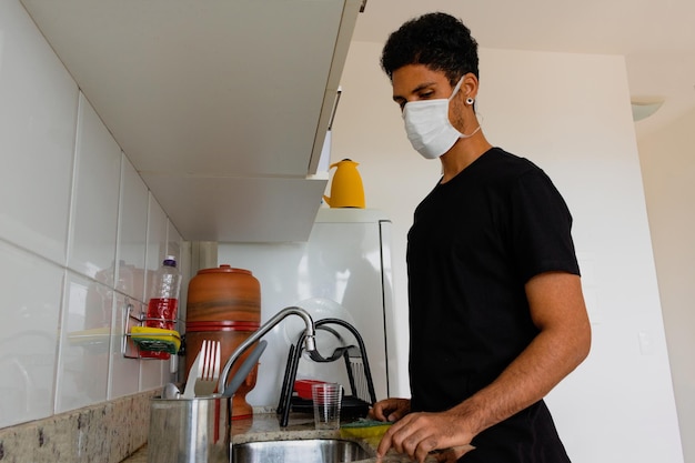Man volwassen zwart met coronavirus masker afwas in de keuken