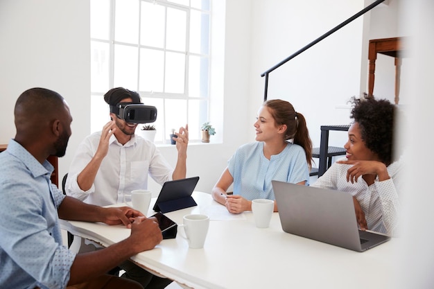 Man in VR goggles at a desk watched by colleagues in office