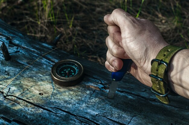 Man vuile hand houdt een mes, een kompas op een oude log in forest.Survival.