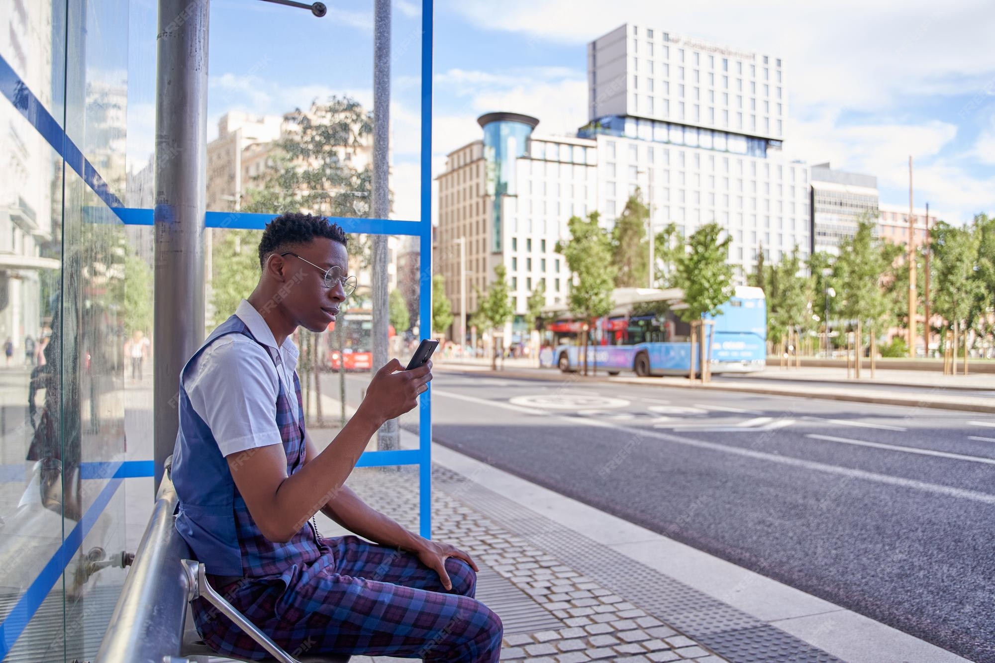 Premium Photo Man waiting at bus stop while looking at smart phone