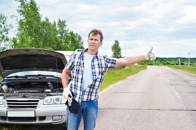 助けを待っていて、車の近くで親指を立てている男性