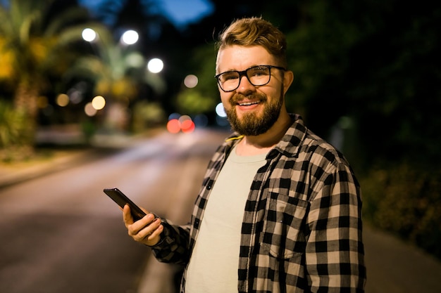 L'uomo attende il taxi utilizzando l'app di trasporto sulle tecnologie delle strade notturne e sul concetto di città