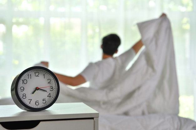 Foto man wakker in de ochtend zittend op bed en stretching, focus op wekker