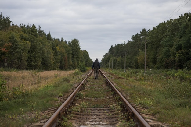 Мужчина уходит по железной дороге с теплым светом Парень-путешественник на железной дороге