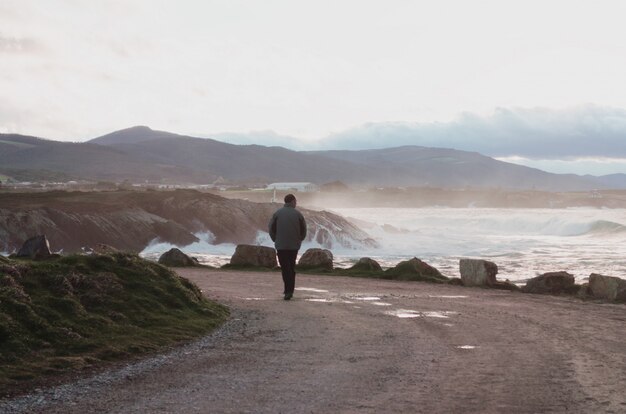 Uomo che cammina lungo la costa in una giornata piovosa con grandi onde.