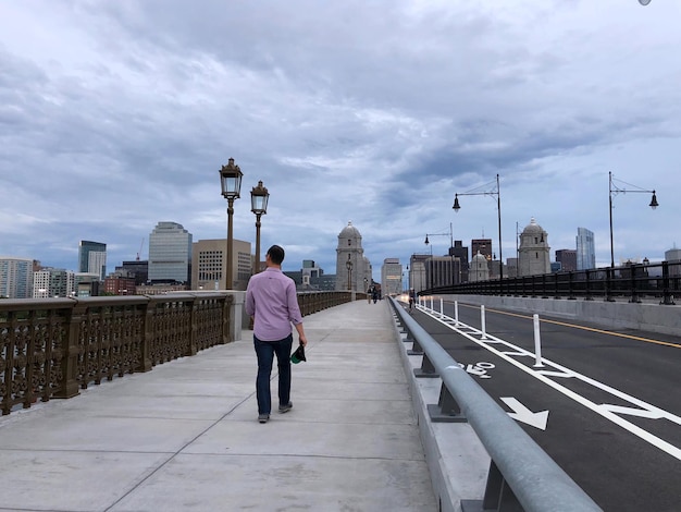 Man walking on bridge in city against sky