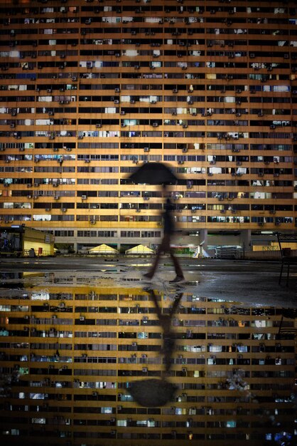 Foto uomo che cammina vicino a una pozzanghera con il riflesso dell'edificio di notte