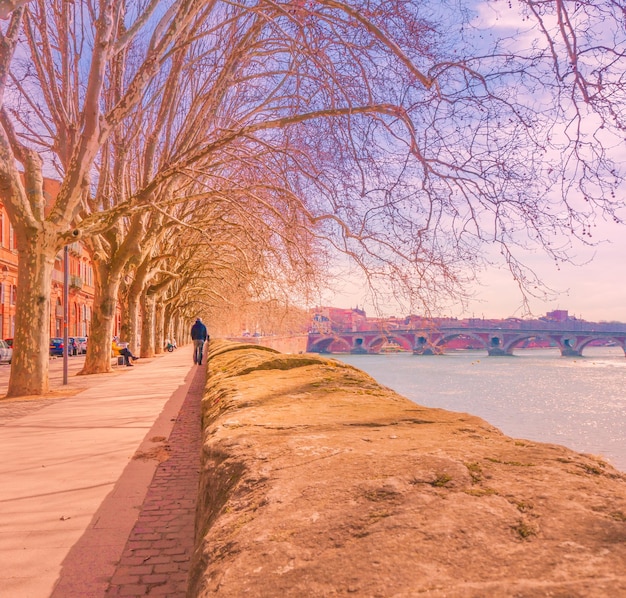 Man walking by river in city during sunset