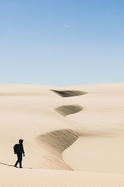 Foto uomo che cammina nel deserto contro un cielo limpido