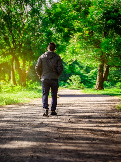 写真 荒れ果てた道を歩いている男、植生に囲まれた道を後ろ向きに歩いている男