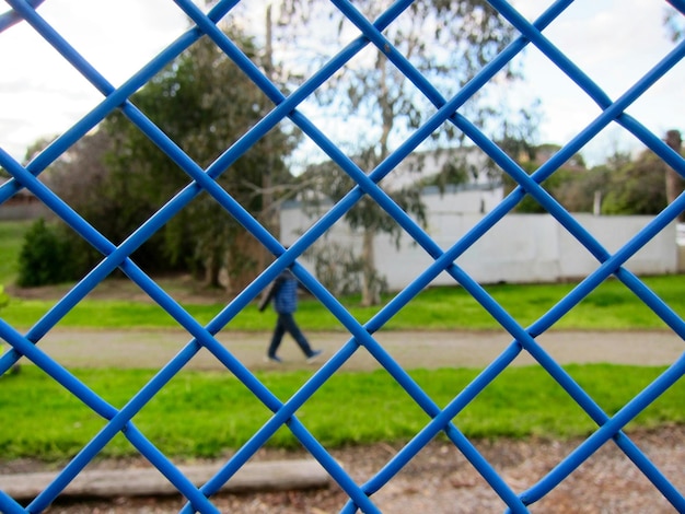 Foto uomo che cammina nel parco visto attraverso la recinzione