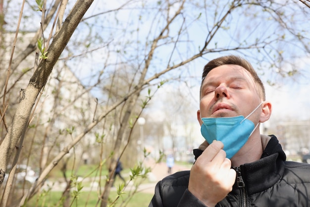 Человек гуляет в парке и снимает защитную маску с лица