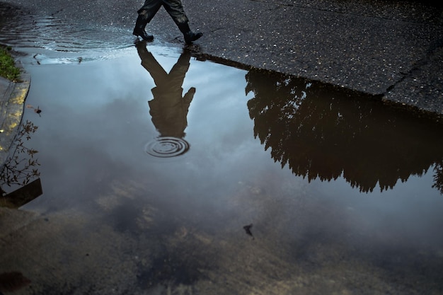 Foto uomo che cammina sulla strada con il riflesso in una pozzanghera