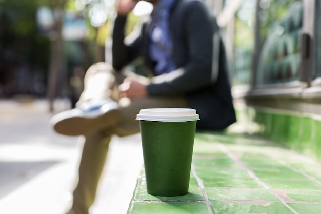 電話で話しているコーヒーを飲みながら通りを歩いている男