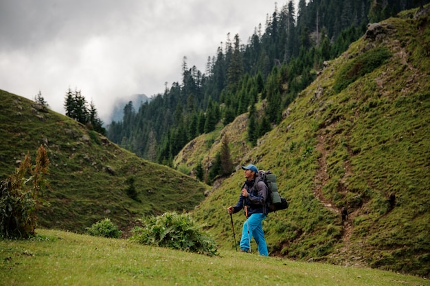 Man walking up the hill with hiking backpack and sticks