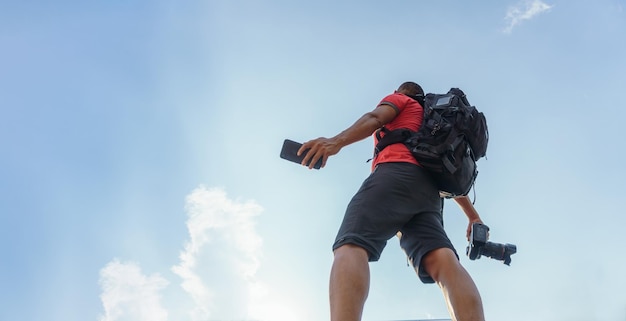 A MAN WALKING WITH A CAMERA IN HAND AND A SMART PHONE