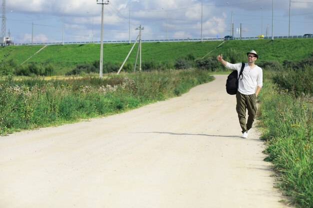 A man walks along a country road. Hitchhiker around the country. A man stops a passing car on the road.