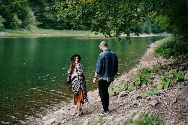 Man walks down to a pregnant woman on the side of a lake in the forest