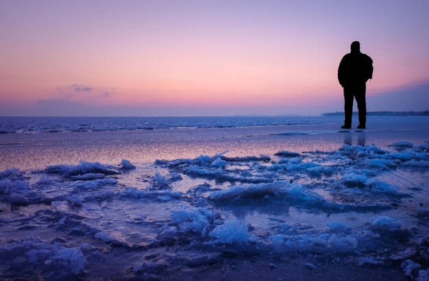 A man walks on the ice on the shore of the sea during the sunrise.