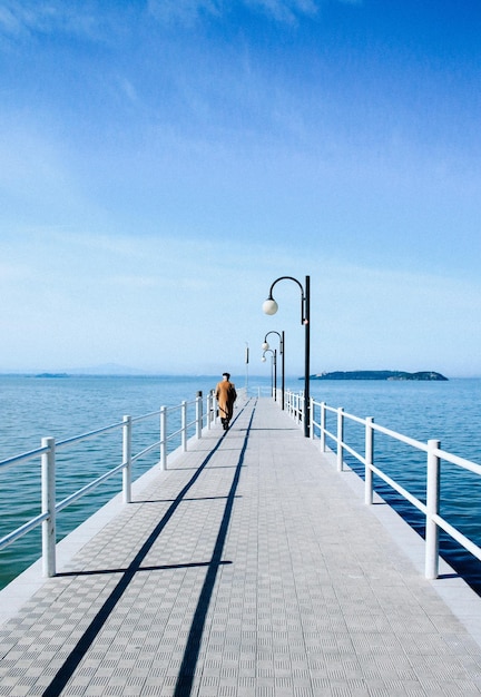 A man walks on a pier with a light post in the background.