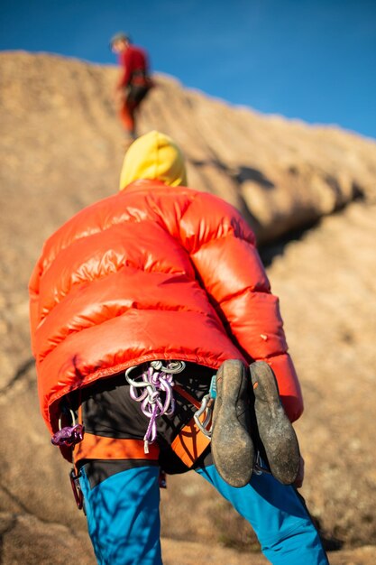 暖かいコートを着た男が見上げ、高い崖の上でクライミングパートナーをチェック