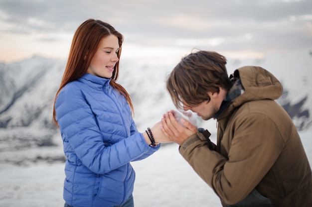 Man warming his girl hands with breathing in mountains