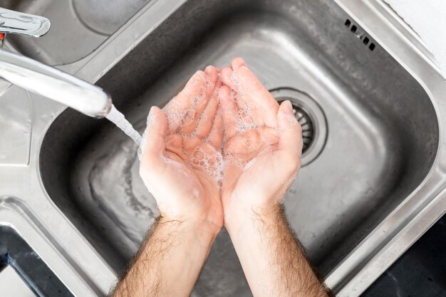 Man wash hands with soap and water in metal sink