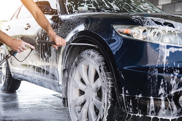 L'uomo lava la schiuma dall'auto con la pressione dell'acqua