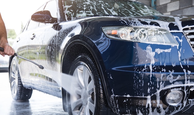 The man washes the foam out of the car with the pressure of water