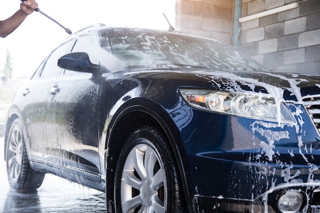 Photo the man washes the foam out of the car with the pressure of water