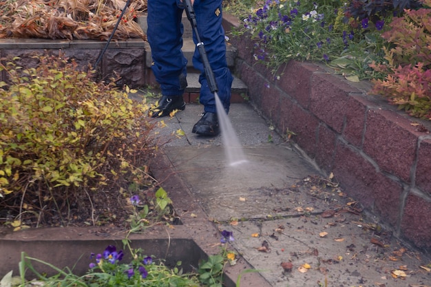 Un uomo lava un sentiero di un giardino con un'idropulitrice. lavori autunnali in giardino.