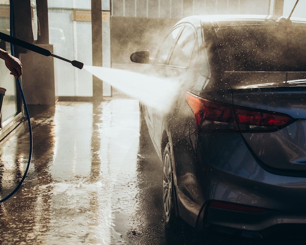 Un uomo lava la sua auto in un autolavaggio self-service usando un tubo con acqua pressurizzata