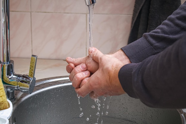 A man washes his hands with soap in the kitchen sink after washing potatoes