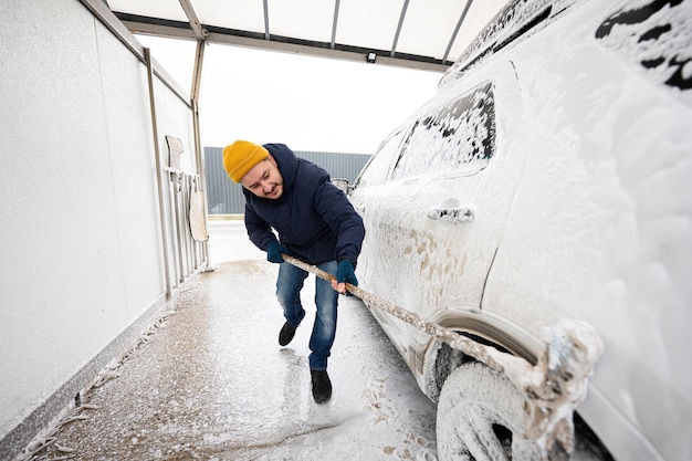 寒い季節にセルフサービスウォッシュでモップでアメリカのSUV車を洗う男