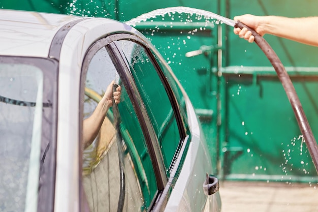 Man washing automobile with water with the hose in the private yard home routines caring for vehicle