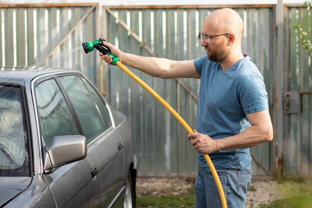 晴れた日に裏庭で噴霧器から水をまき散らして洗車する男性