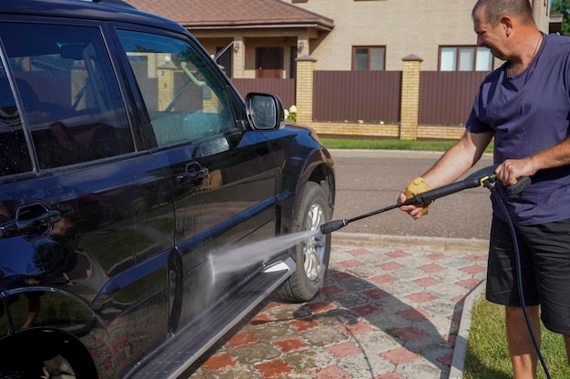 Мужчина моет машину с помощью машины для мытья под давлением, шампуня, губки и полотенца из микрофибра