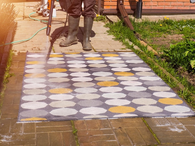 Man washing carpet with pressure washer outdoors